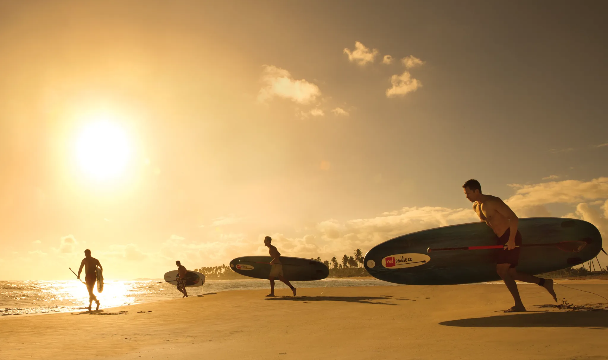 Friends running to the ocean at sunset with peddle boards